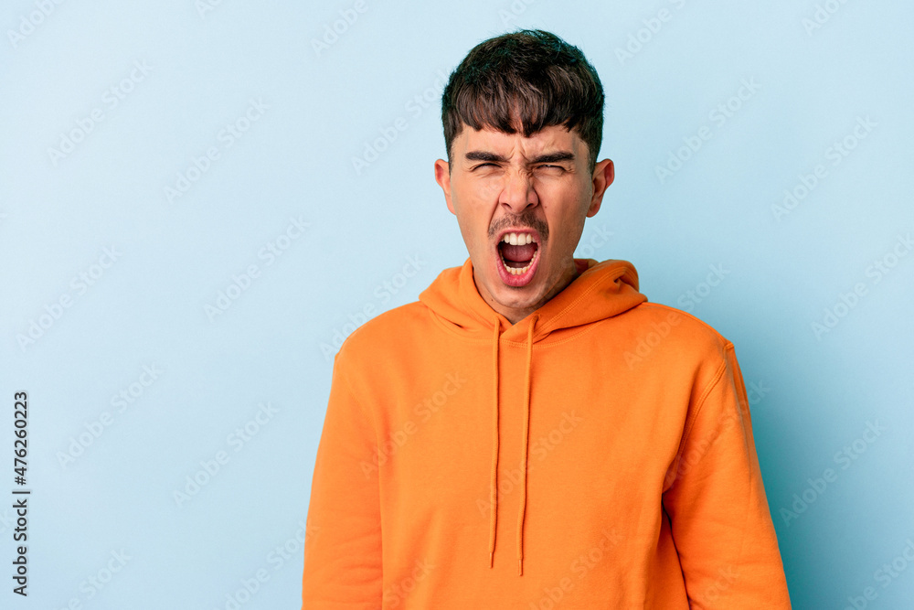Young mixed race man isolated on blue background shouting very angry, rage concept, frustrated. Young mixed race man isolated on blue background shouting very angry, rage concept, frustrated.