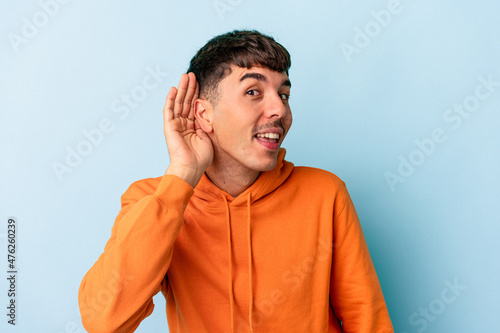 Young mixed race man isolated on blue background trying to listening a gossip.