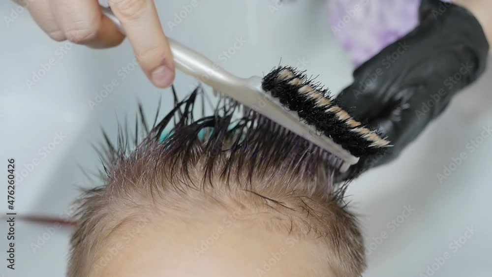A hair dye expert applies purple dye to the hair with a special comb