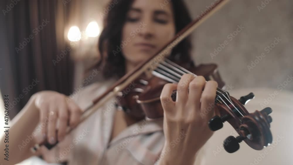 beautiful girl playing the violin while sitting on the bed at home, hand-held shooting, close-up beautiful girl playing the violin while sitting on the bed at home, hand-held shooting, close-up