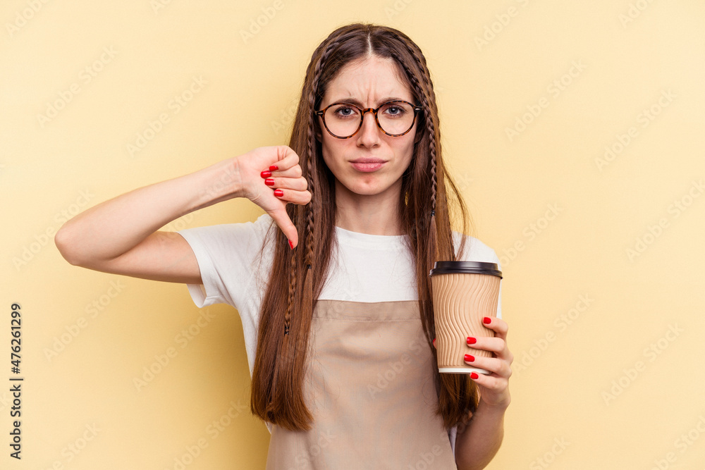 Restaurant waiter woman holding a take away coffee isolated on yellow background showing a dislike gesture, thumbs down. Disagreement concept. Restaurant waiter woman holding a take away coffee isolated on yellow background showing a dislike gesture, thumbs down. Disagreement concept.