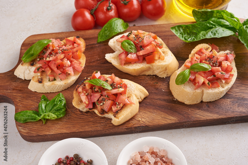 Tasty savory tomato Italian appetizers, or bruschetta, on slices of toasted baguette garnished with basil, vegetables, herbs on grilled or toasted crusty ciabatta bread.