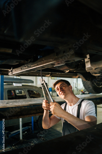Vertical portrait of serious handsome professional male car mechanic in uniform standing in inspection pit and working with tool. Concept of car service, repair and maintenance.