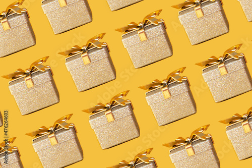 Shiny silver gift box with golden bow on bright gold background. Holiday concept. Pattern
