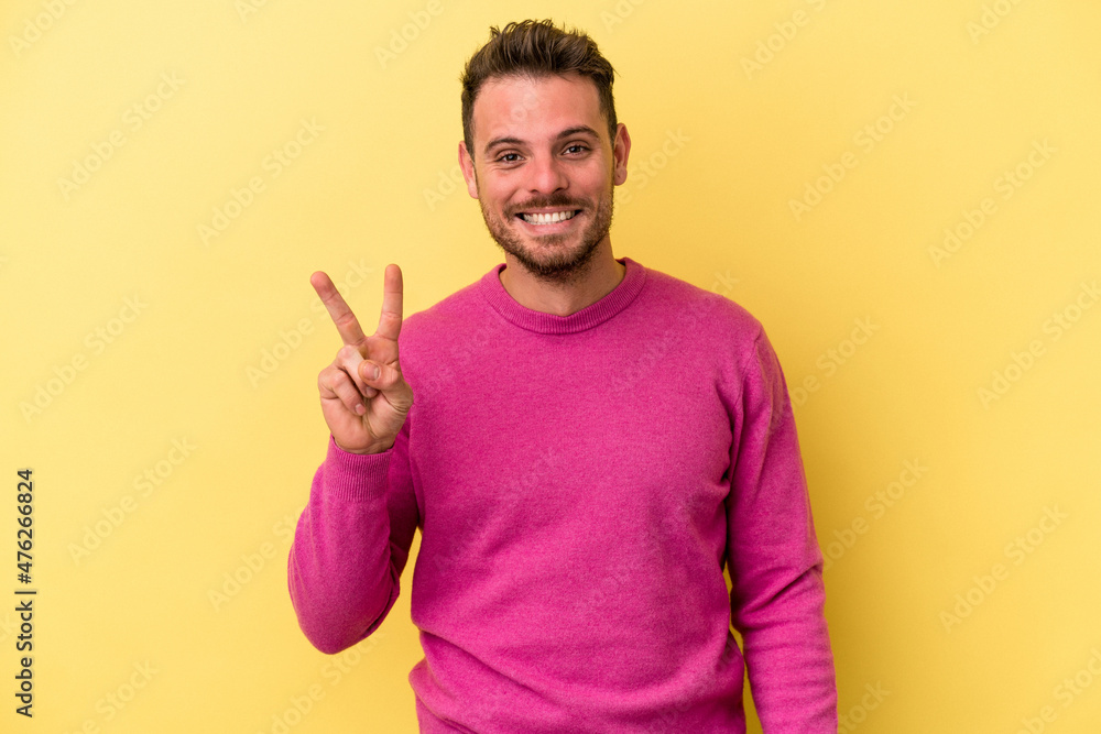 Young caucasian man isolated on yellow background showing victory sign and smiling broadly. Young caucasian man isolated on yellow background showing victory sign and smiling broadly.