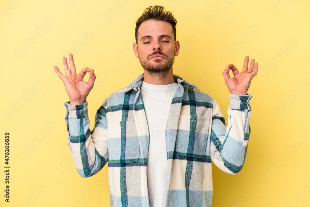 Naklejka premium Young caucasian man isolated on yellow background relaxes after hard working day, she is performing yoga.