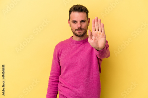 Young caucasian man isolated on yellow background standing with outstretched hand showing stop sign, preventing you.