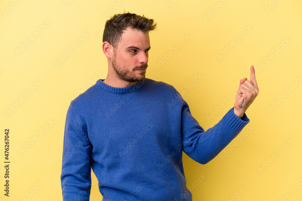 Young caucasian man isolated on yellow background pointing with finger at you as if inviting come closer. Young caucasian man isolated on yellow background pointing with finger at you as if inviting come closer.