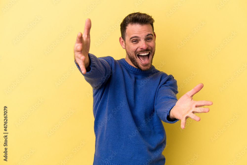 Young caucasian man isolated on yellow background feels confident giving a hug to the camera. Young caucasian man isolated on yellow background feels confident giving a hug to the camera.