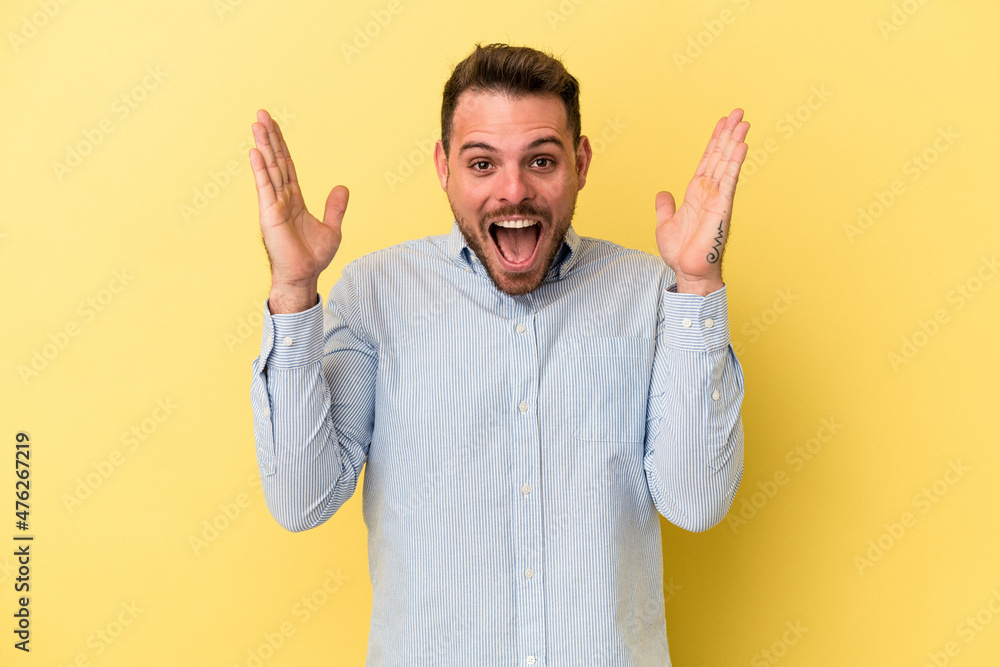 Fototapeta premium Young caucasian man isolated on yellow background receiving a pleasant surprise, excited and raising hands.