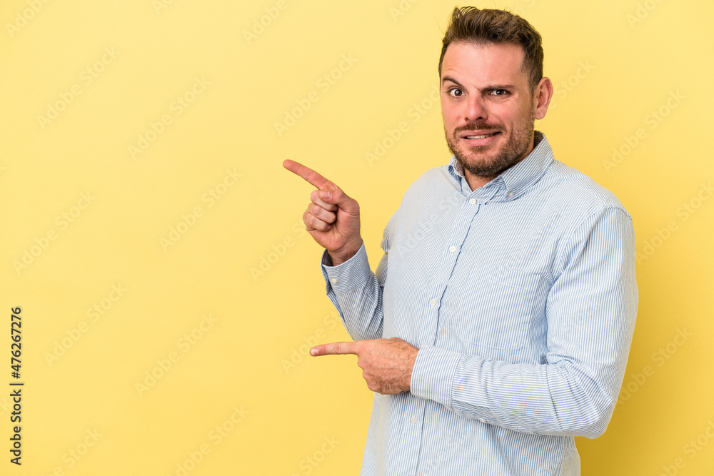 Young caucasian man isolated on yellow background shocked pointing with index fingers to a copy space. Young caucasian man isolated on yellow background shocked pointing with index fingers to a copy space.