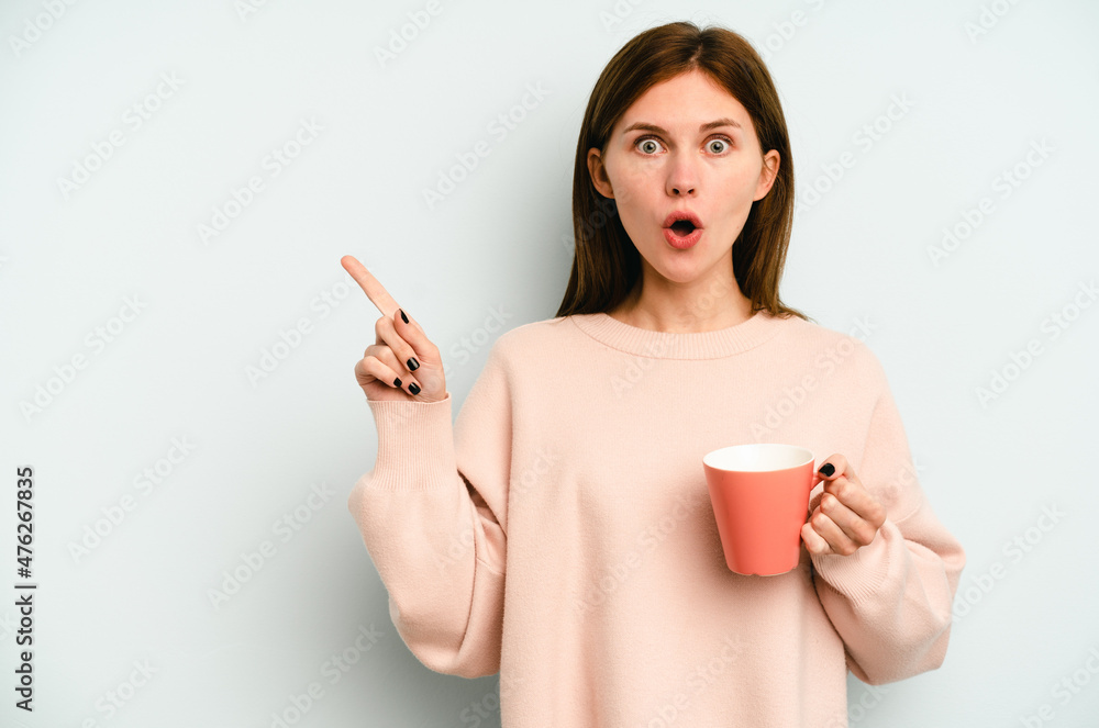 Young English woman holding a mug isolated on blue background pointing to the side Young English woman holding a mug isolated on blue background pointing to the side