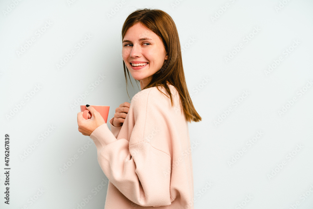 Young English woman holding a mug isolated on blue background looks aside smiling, cheerful and pleasant. Young English woman holding a mug isolated on blue background looks aside smiling, cheerful and pleasant.