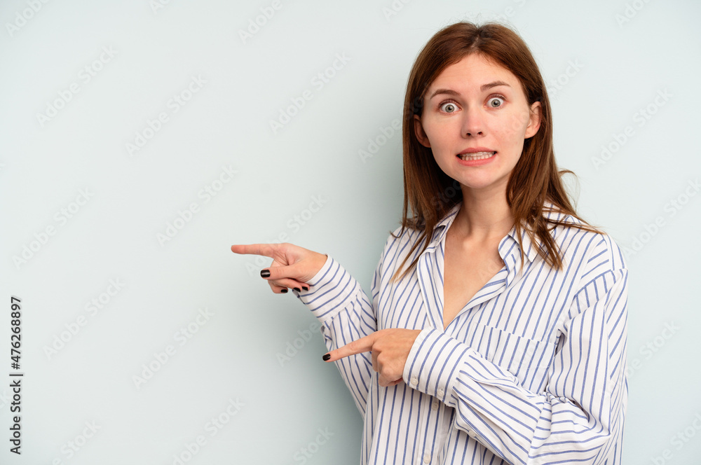 Young English woman isolated on blue background shocked pointing with index fingers to a copy space. Young English woman isolated on blue background shocked pointing with index fingers to a copy space.