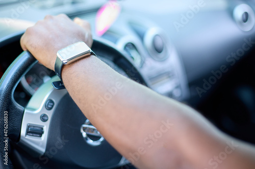 The left hand of a black man on the steering wheel of a car. An African man in a smart watch drives a car