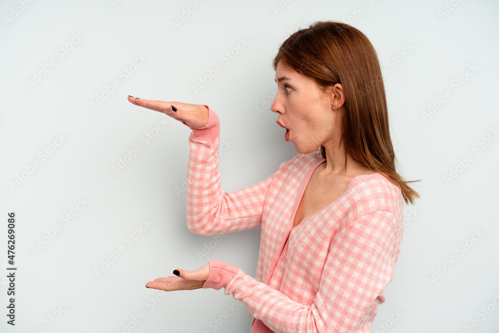 Young English woman isolated on blue background shocked and amazed holding a copy space between hands. Young English woman isolated on blue background shocked and amazed holding a copy space between hands.