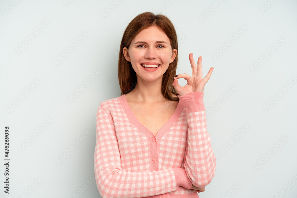 Young English woman isolated on blue background winks an eye and holds an okay gesture with hand.