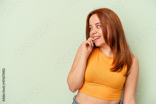 Young caucasian woman isolated on green background relaxed thinking about something looking at a copy space.