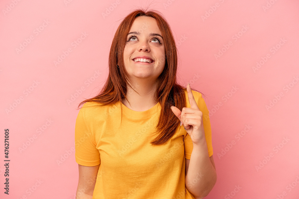 Young caucasian woman isolated on pink background indicates with both fore fingers up showing a blank space. Young caucasian woman isolated on pink background indicates with both fore fingers up showing a blank space.