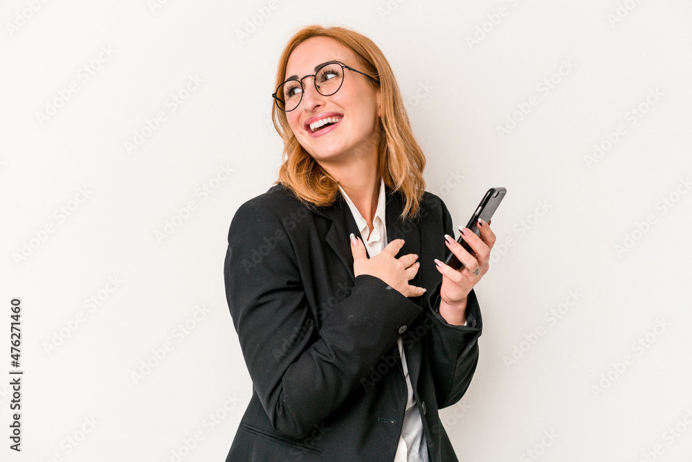 Young business caucasian woman holding mobile phone isolated on white background looks aside smiling, cheerful and pleasant. Young business caucasian woman holding mobile phone isolated on white background looks aside smiling, cheerful and pleasant.