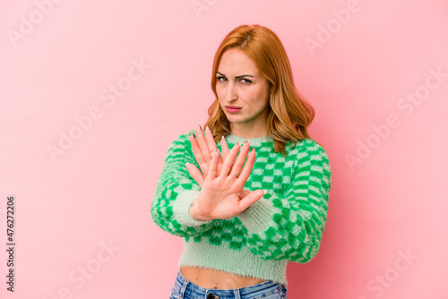 Young caucasian woman isolated on pink background standing with outstretched hand showing stop sign, preventing you.