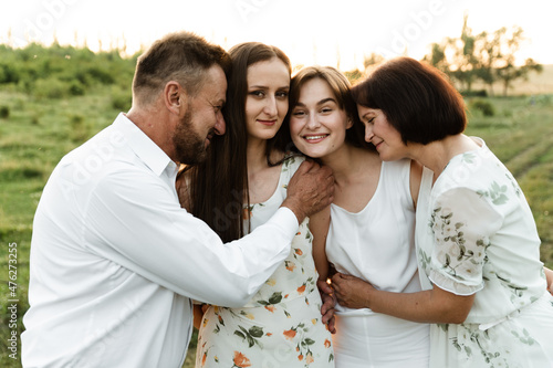 father and mother of middle age tenderly hug two adult daughters in nature. beautiful family walks across the field at sunset of the day. parents with older children