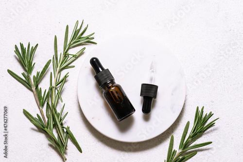 Rosemary essential oil in glass bottle with dropper and fresh green rosemary twigs on white marble background top view. Natural cosmetic ingredients.
