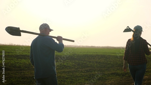 Fotografie, Obraz Farmers in boots walk with tools with shovels, hoe across field with green shoots