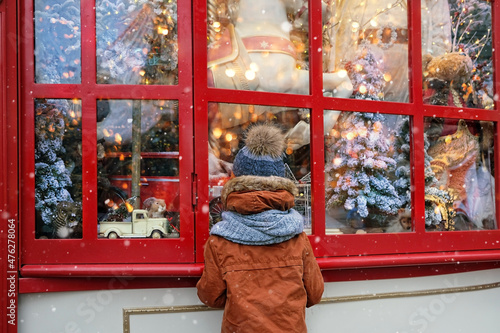 boy watching festive window display at gift store.  New Year and Christmas holidays concept. Child and christmas shop window. winter season