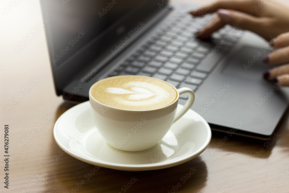 Working process on lapton in the morning and taking a coffee at the cafe. Lapton and a cup of coffee is standing on the wooden table. Working process on lapton in the morning and taking a coffee at the cafe. Lapton and a cup of coffee is standing on the wooden table.