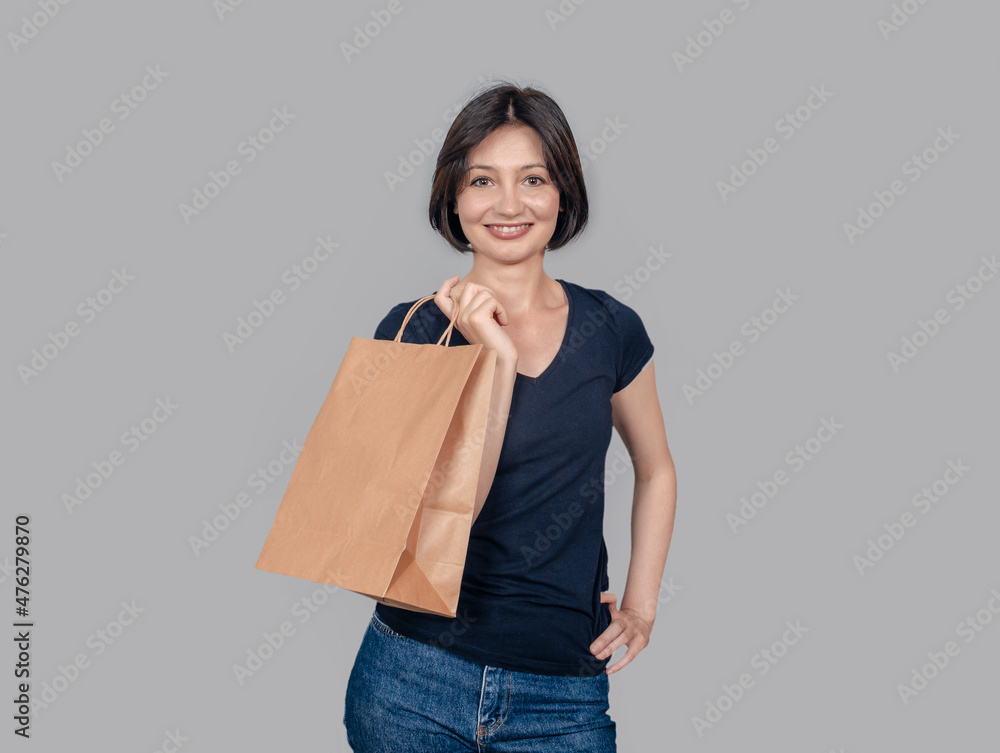 Studio portrait of charming woman in casual clothes laughing and holding a paper bag. Gray background. Studio portrait of charming woman in casual clothes laughing and holding a paper bag. Gray background.