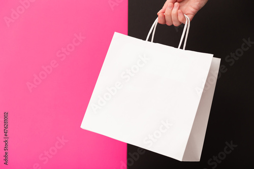 Female hand holding white blank shopping bag isolated on pink and black background. Black friday sale, discount, recycling, shopping and ecology concept.