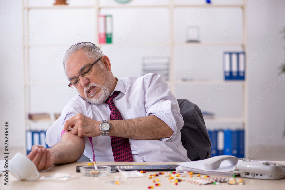 Old drug addicted employee sitting in the office - obrazy, fototapety, plakaty 