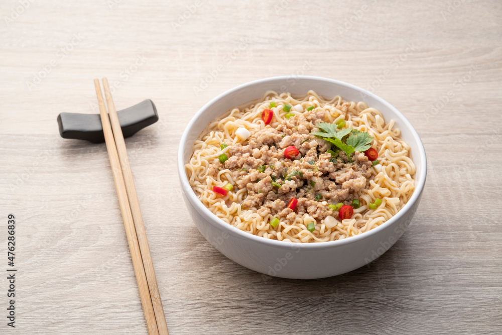 Instant noodle soup with minced pork in white bowl on wood table Instant noodle soup with minced pork in white bowl on wood table