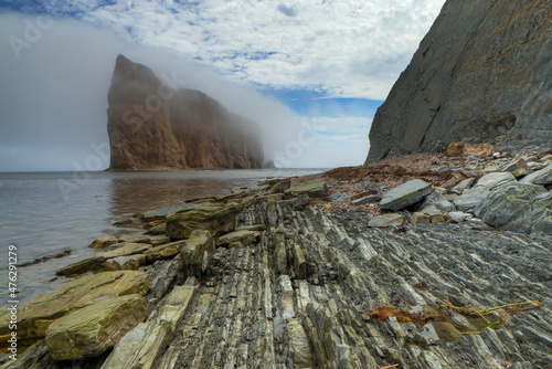 Beautiful shot of fog covering the Perce Rock formations under a blue cloudy sky photo