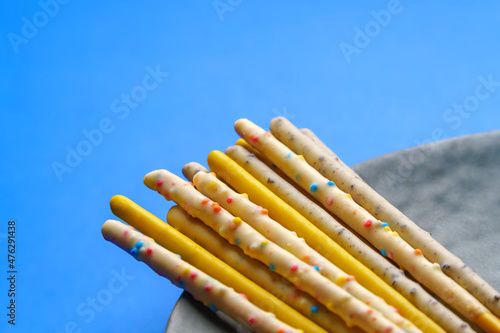 Sweet straw covered with multi-colored glaze with additives. On a gray plate and a blue background. photo