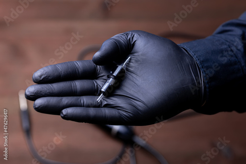 the hands of a permanent makeup artist in black medical gloves on which lies a disposable cartridge for a tattoo machine