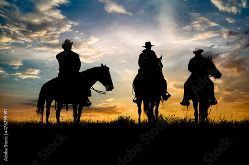 Three cowboys silhouetted against dawn sky