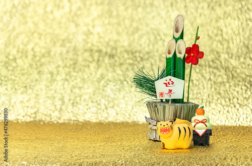 Japanese New Year's Greeting Card of a bamboo kadomatsu with the words congratulations for the welcoming spring, a kagami mochi rice cake and a cute figurine of a roaring tiger on a golden background. photo