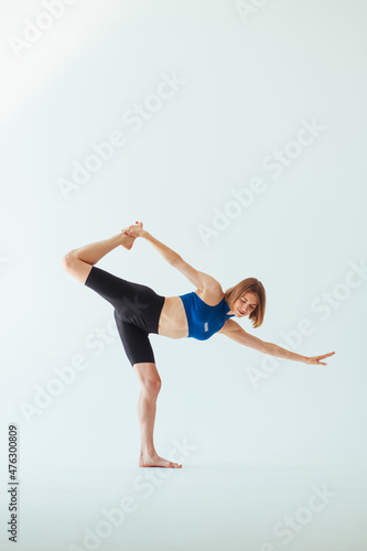 Beautiful sports woman in blue dill is darkened by stretching on a white background. Lady is doing yoga