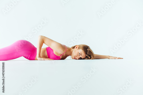 Beautiful sports woman in pink clothes lies on a white background during somatics and poses for the camera. photo