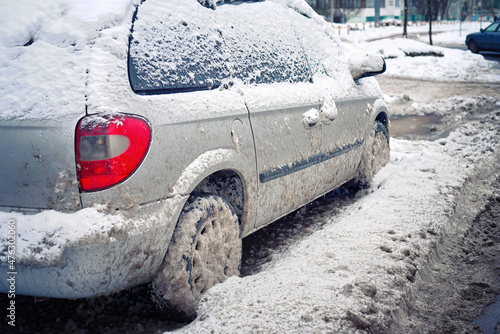 Snow covered car parked at roadside. Blocked car in dirty snowdrift on roadside in the city after snow removal by municipal services.