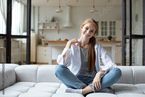 Portrait of happy redhead woman sitting on sofa at home, daydreaming.