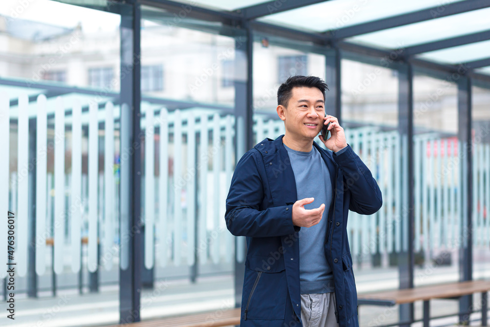 Cheerful and happy Asian businessman talking on the phone, waiting for a plane and a taxi at a public transport stop Cheerful and happy Asian businessman talking on the phone, waiting for a plane and a taxi at a public transport stop