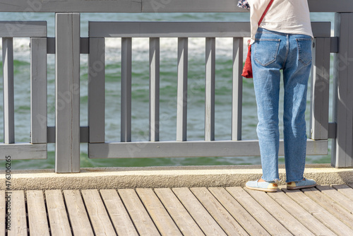 The girl's legs are close-up at the railing of the embankment of the reservoir. © YuNIK