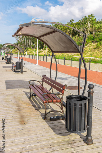 A wooden bench under a canopy from the sun with an urn on the embankment.