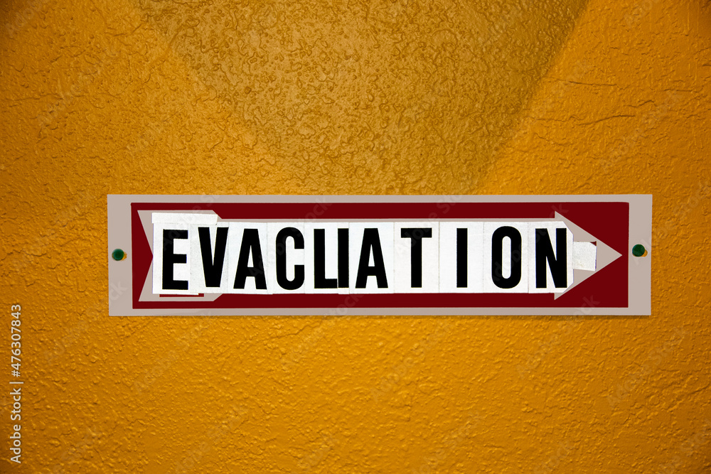 Obraz premium Evacuation Sign- hobbled together from some other kind of sign and stick on letters - tacked to orange stucco wall.