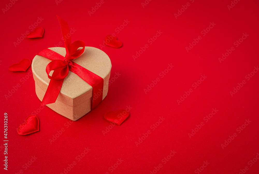 Beautiful minimal wrapped gift box heart shaped with red bow ribbon on red background and small padded hearts top view flat lay, present for Saint Valentine day, love and relationship, space for text