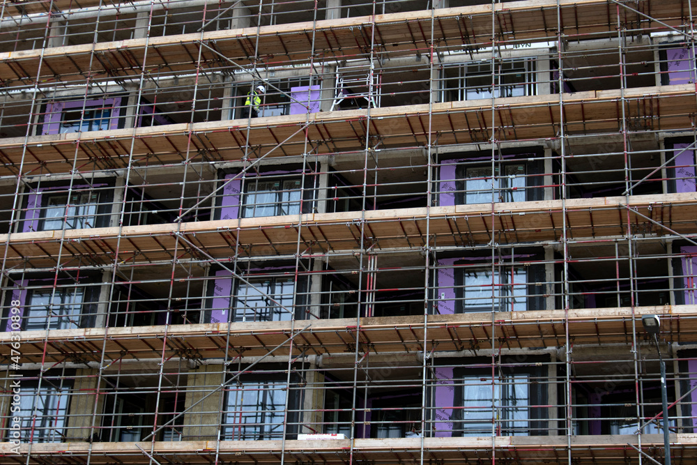 Scaffolding on a multi-story building, worker with high vis vest and a hard hat