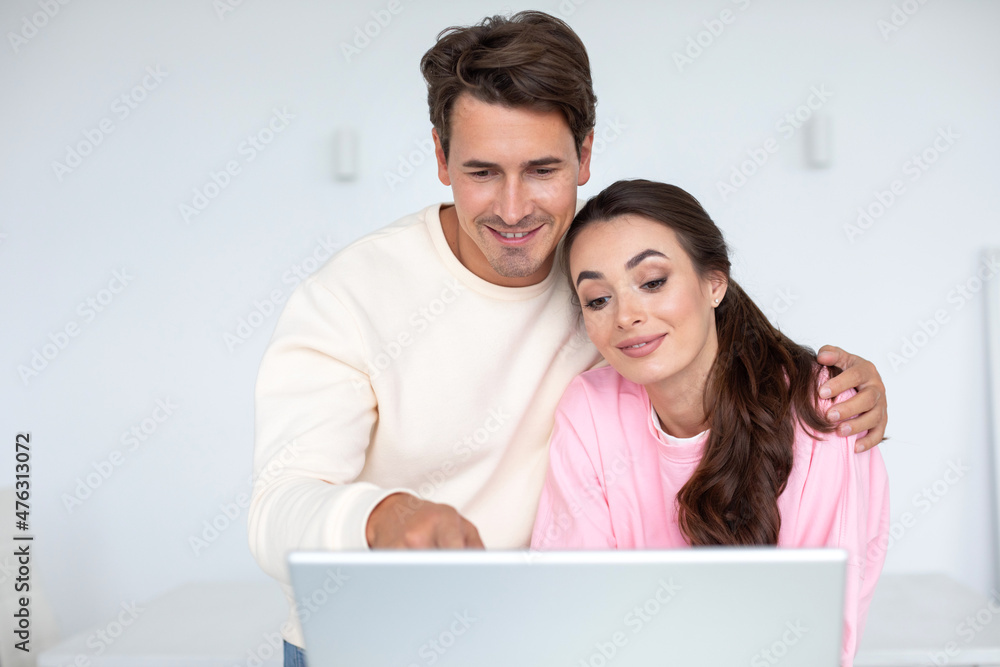 Happy young couple planning budget, smiling woman and man looking at laptop screen at home together. Happy young couple planning budget, smiling woman and man looking at laptop screen at home together.